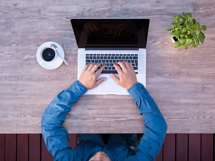 Estimer votre site web en ligne, simplement Personne travaillant sur un ordinateur portable, vue de dessus, avec un café.