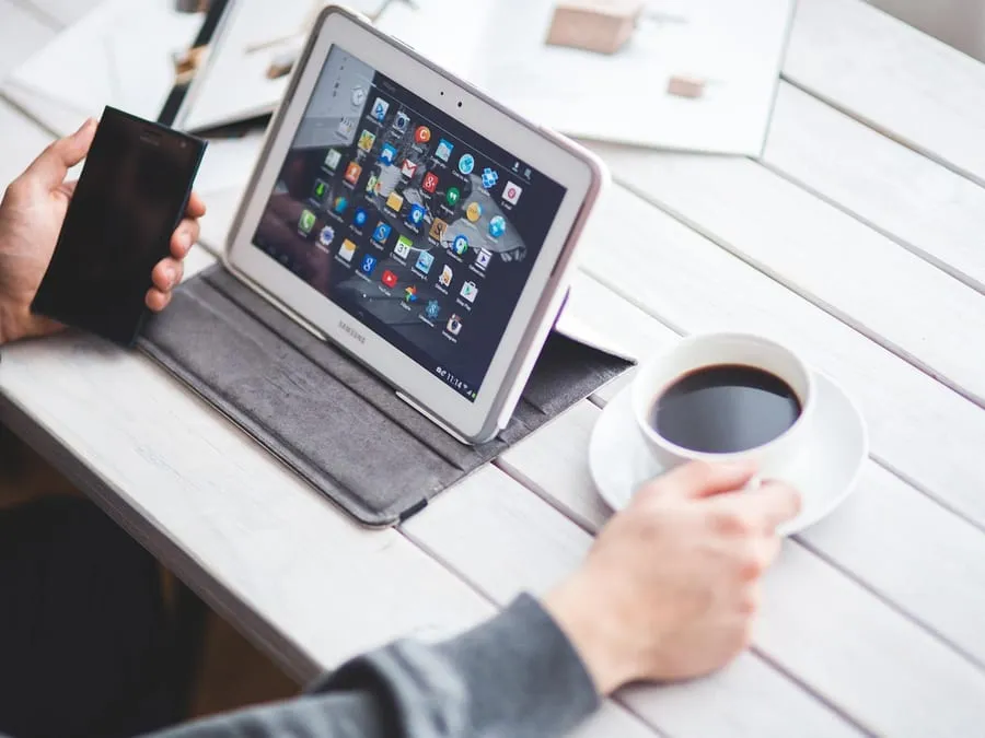 Ce qui détermine le prix d'une application mobile Main tenant un smartphone à côté d’une tablette posée sur un bureau.