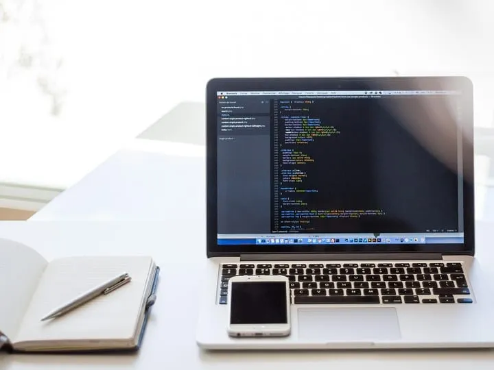 Poste de travail du studio : ordinateur affichant du code et carnet de notes.